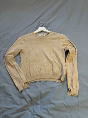 Beige stickad tröja från Pull&Bear - En stilren beige croppad stickad tröja från Pull&Bear  med rund halsringning och långa ärmar. Tröjan har ribbade muddar vid ärmslut och nederkant, perfekt för en enkel och clean look.