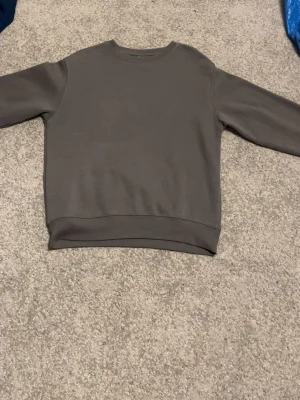 Grå basic sweatshirt - Aldrig  använd också en enkel och stilren grå sweatshirt med rund hals och långa ärmar. Tröjan har ribbade muddar vid ärmslut och nederkant. Perfekt för en avslappnad och clean look. Materialet känns mjukt och bekvämt mot huden.