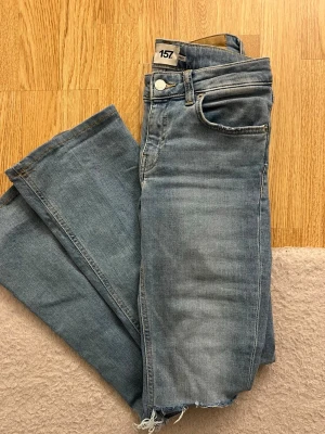 Ljusblå bootcut jeans med slitna knän - Snygga ljusblå bootcut jeans med råa, slitna knän och fransig kant. Klassisk femficksmodell och normal passform. Perfekta för en avslappnad och trendig look. Tillverkade i mjukt bomullsjeansmaterial.