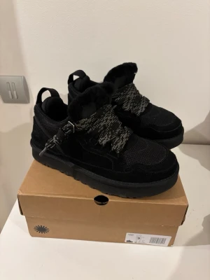 UGG lowmels - Säljer ett par svarta UGG lowmels med grov sula och snörning. Skorna har en blandning av mocka och textilmaterial samt mönstrade skosnören. Perfekta för dig som vill ha något både snyggt och bekvämt. Extremt bra skor till kallt väder och kyliga dagar❄️