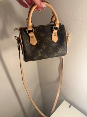 Mini Speedy - Andra väskor uppe på min sida!  Säljer en klassisk handväska i brunt med ikoniskt monogrammönster. Väskan har både handtag och avtagbar axelrem i beige skinn samt guldfärgade metalldetaljer. Använd ett fåtal gånger och är i otrolig kvalitet!☀️