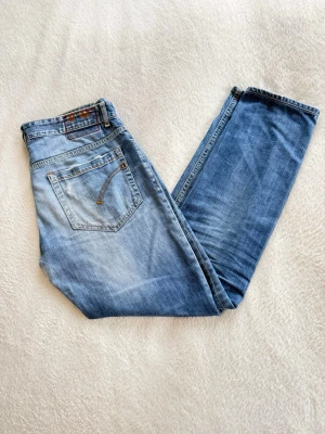 Blå jeans från Dondup med knappar - Snygga blå jeans från Dondup med klassisk femficksmodell och knappgylf. Jeansen har en ljus tvätt med subtila slitningar och kontrastsömmar. Perfekta för dig som gillar en avslappnad men stilren look. Materialet är jeans i bomull.