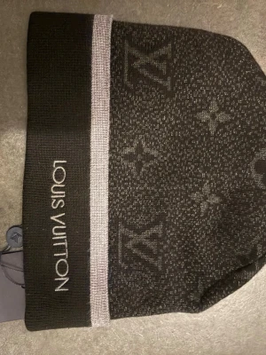 Svart exklusivt mössa - Snygg svart mössa från lui ton med klassiskt monogrammönster och vit rand. Broderad logga framtill. Perfekt accessoar för att lyfta din outfit med exklusiv känsla. Stickad i mjukt material som håller dig varm.