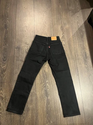Svarta Levi's 501 jeans  - Snygga svarta Levi's 501 jeans med klassisk straight fit och femficksmodell. Jeansen har den ikoniska läderpatchen bak i midjan och röd Levi's-tagg på bakfickan. 