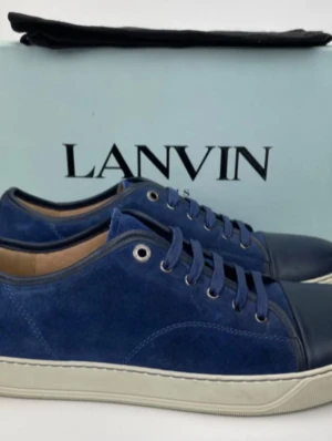 Blå mocka sneakers från Lanvin - Snygga blå sneakers från Lanvin i mocka med matchande blått skinn på tån och vita sulor. Klassisk låg modell med snörning och metallöljetter. Perfekta för dig som vill ha en stilren och exklusiv sneaker med premiumkänsla.