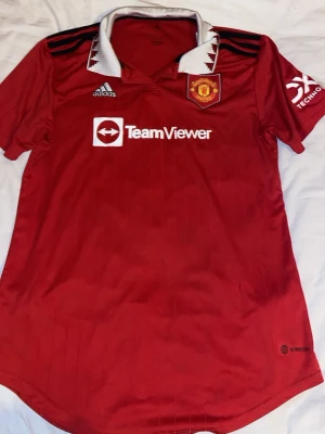 Manchester United matchtröja Adidas M - Röd Manchester United matchtröja från Adidas med vit krage och svarta detaljer. Broderad klubbmärke på bröstet, TeamViewer-logga och Adidas-logga. Tillverkad i funktionsmaterial, perfekt för fotboll eller träning. Extremt bra skick för ett ny pris av 1300kr. Användt kanske 6-7 gånger. Säljer då jag blivit ett arsenal fan:)