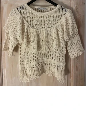 Beige virkad topp med volang - Supersöt beige virkad topp från Zara med volangdetaljer över bröstet och ärmarna. Kort ärm och rund halsringning. 