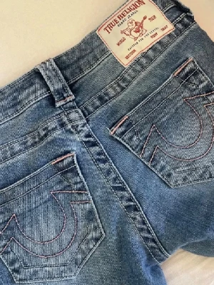 Blå True Religion jeans med rosa sömmar - Säljer ett par jeans från True Religion. Säljs inte längre. Egen uppsydda så passar någon som är runt 160!