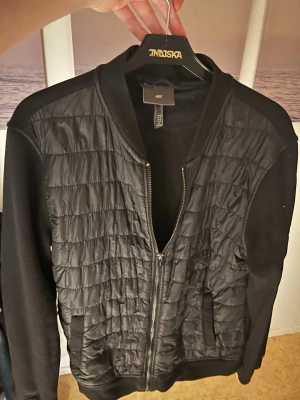 Vårjacka från HM - Säljer en svart bomberjacka från H&M i storlek M. Jackan har quiltad framsida i blankt material och släta svarta ärmar. Använd ett par gånger men inget man märker. Använder inte den längre så säljer den vidare till någon annan. Mitt pris 199kr. Kontakta mig om du har frågor.