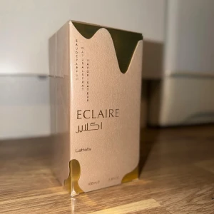Lattafa Eclaire Eau de Parfum - Lattafa Eclaire Eau de Parfum kommer i en elegant beige och guldfärgad förpackning med stilren design. Flaskan rymmer 100 ml och har en lyxig känsla med moderna detaljer. Perfekt för dig som gillar exklusiva dofter och snygg design på parfymflaskan.