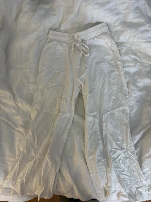 Vita linnebyxor från Soyaconcept - Säljer ett par vita linnebyxor från Soyaconcept med resår och knytband i midjan. Byxorna har raka ben och avslappnad passform, perfekta för varma dagar. Luftigt material som känns skönt mot huden. Korta i passformen