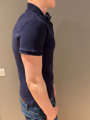 Mörkblå pikétröja i bomull - Klassisk mörkblå pikétröja med krage och korta ärmar. Tillverkad i mjuk bomull som sitter snyggt och har en slim passform. Perfekt till jeans eller chinos för en clean look.