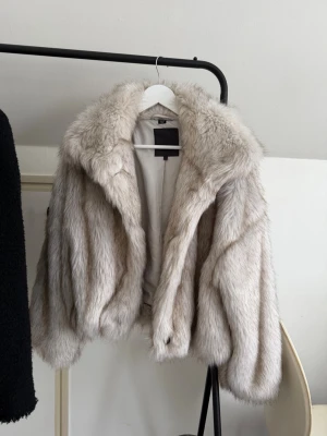 Beige pälsjacka med bred krage - Snygg beige pälsjacka med bred krage och voluminös passform. Jackan har en klassisk look med mjuk pälsimitation och är perfekt för att höja din outfit. Stängs framtill och har långa ärmar. Perfekt för dig som vill sticka ut med en trendig jacka. Pris kan diskuteras!