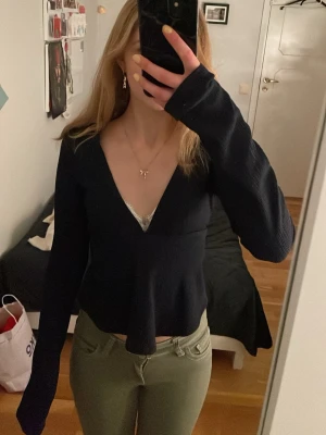 Mörkblå topp med v-ringning - Snygg mörkblå urringad topp med v-ringning och långa ärmar. Toppen har en lätt utsvängd nederdel och markerad midja, vilket ger en smickrande siluett. Perfekt att styla med jeans eller kjol för en trendig look. I princip oanvänd då den är lite för kort för min överkropp💞