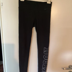 Svarta Nike Dri-Fit leggings S - Svarta leggings från Nike med Dri-Fit-teknologi och diskret Swoosh-logga på höften. Tight passform och hög midja, perfekta för träning eller chill. Snyggt tryck längs benet och stretchigt material som andas.