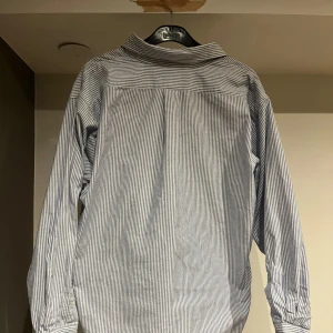 Randig skjorta från Ralph Lauren - Säljer en klassisk blå- och vitrandig skjorta från Ralph Lauren i 100% bomull. Skjortan har långa ärmar och en broderad logotyp på bröstet. Perfekt för en stilren look! Skjortan är i väldigt bra skick och knappast använd. Bara att höra av sig vid eventuella frågor!☺️