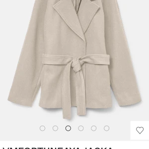 Beige kappa med bälte och krage - Stilren beige kappa med klassisk krage och knytskärp i midjan. Jackan har lång ärm och rak passform, perfekt för dig som gillar en clean och tidlös look. Materialet ser ut att vara ullblandning som ger en mjuk och lyxig känsla.
