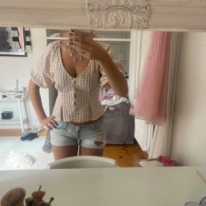 Beige och vit rutig blus - Supersöt blus från Bik Bok i beige och vitt rutigt mönster. Modellen har puffiga korta ärmar, v-ringning och knappar framtill. Perfekt till vardags men också finare tillfällen🤎🤎🤎defekt på bild 3 men inget som syns på!!