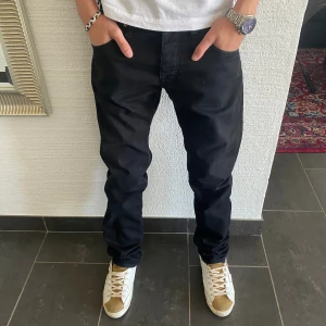 Tiger Of Sweden Jeans - Svarta jeans från Tiger Of Sweden i storlek 30/32. Klassisk femficksmodell med raka ben och normal passform. Snygga detaljer med svarta sömmar och diskret läderpatch bak i midjan. Perfekta svarta jeans för en clean look.