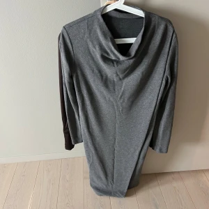 Grå långärmad klänning med polokrage - En enkel och stilren grå klänning med lång ärm och lös polokrage. Klänningen har rak passform och är tillverkad i ett mjukt, stretchigt material som känns bekvämt mot huden. Med ”lös häng del” fram. Perfekt för dig som gillar minimalistisk och clean stil.