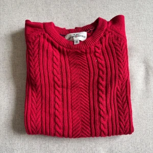 Röd kabelstickad tröja Hampton Republic - Snygg röd kabelstickad tröja från Hampton Republic med klassiskt mönster och rund hals. Tröjan har långa ärmar och ribbade muddar vid ärmslut och nederkant. Perfekt för kyligare dagar 