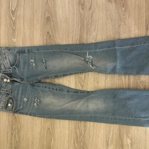 Blå bootcut jeans med slitningar - Snygga lågmidjade jeans från Gina Tricot Young i storlek 158. Jag har sprättat ner sömmen längst ner så de är några cm längre. Har även gjort egna hål fram och på ena bak fickan. De är väl använda men i bra skick, men är lite smutsiga längst ner  💗 bootcut 