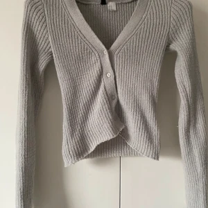 Ljusgrå ribbad kofta från H&M Divided - Superfin ljusgrå ribbad kofta från H&M Divided i storlek XS. Koftan har v-ringning, knappar framtill och är långärmad. perfekt att slänga på sig över ett linne eller t-shirt.