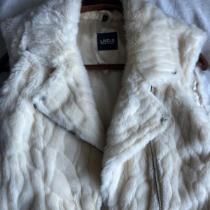 Vit pälsväst från Livelo - Snygg och fluffig vit pälsväst från Livelo med bred krage och dragkedja framtill. Super skön!! I storlek M😊