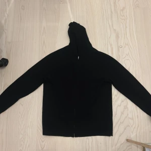 Svart hoodie med dragkedja - En klassisk svart hoodie med dragkedja framtill och huva. Tröjan har lång ärm och en enkel, stilren design som passar till det mesta. Perfekt för dig som gillar en avslappnad och clean look.