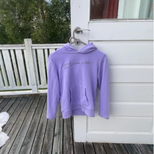 Ljuslila hoodie från Champion - Säljer en ljuslila hoodie från Champion med broderad logga på bröstet. Köpt från kids brandstore. Tröjan har huva, magficka och långa ärmar!💜