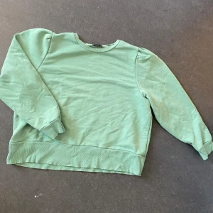 Mintgrön sweatshirt med puffärm - En mintgrön sweatshirt från Lindex med puffiga axlar och rund halsringning. Tröjan har långa ärmar och ribbade muddar vid ärmslut och nederkant. Perfekt för dig som gillar en chill och trendig look.