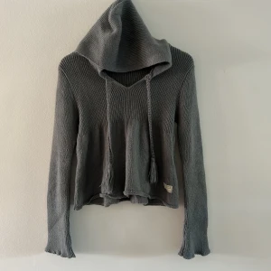 Grå stickad hoodie från Odd Molly - Mysig grå stickad hoodie från Odd Molly med långa ärmar, v-ringning och snörning med tofsar. Tröjan har en avslappnad passform och är perfekt för kyliga dagar. Snygg detalj med etikett nertill och ribbade muddar. Är lite nopprig, men fin 