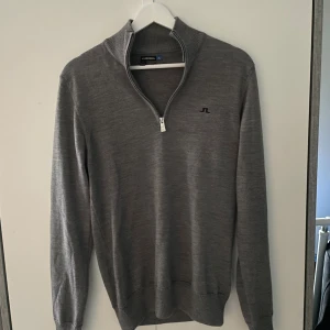 J.Lindeberg tröja - Hej! Snygg grå långärmad tröja från J.Lindeberg med half zip och diskret JL-logga på bröstet. Tröjan är stickad i mjukt material och har ribbade muddar vid ärmslut och nederkant. Perfekt för lager-på-lager och stilren look.