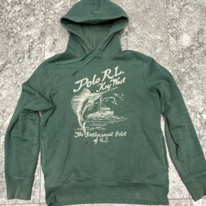  Polo Ralph Lauren Key West - Snygg grön hoodie från Polo Ralph Lauren med tryck 'Polo R.L. Key West'. Den är i bra skick, skulle säga 8/10. Storlek M. Liten fläck på magen.