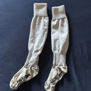 Vita fotbollsstrumpor från Macron - Långa vita fotbollsstrumpor från Macron med ribbade partier och förstärkt struktur vid vrist och fot. Dom är storlek 38-39 men dom är ju stretchiga så dom passar nog upp till 40. 