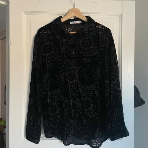 Svart sammetsskjorta från NA-KD - Säljer en svart skjorta från NA-KD i sammet med blommigt mönster. Skjortan har klassisk krage, knappar framtill och långa ärmar. 