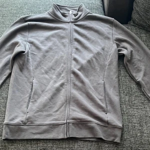 Grå ziptröja från Dressmann - Grå långärmad ziptröja från Dressmann i storlek M. Tröjan har hel dragkedja framtill, ståkrage och två sidofickor. Mjuk och skön bomullskänsla, perfekt för chill eller när du vill ha en enkel look.