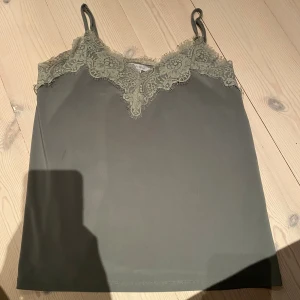 Grön linnetopp med spets från Amisu - Snygg grön linnetopp från Amisu i storlek XS. Toppen har tunna axelband och vacker spetsdetalj längs urringningen. Perfekt att styla med jeans eller kjol för en trendig look.