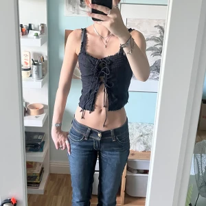 Svart korsettopp från Gina Tricot - Svart korsettopp från Gina Tricot med snörning framtill och volangkant längs axelband. Knappt använd och i fint skick :)