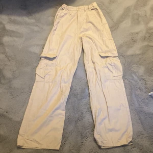 Beiga cargobyxor från H&M, stl 170 - Snygga beiga cargobyxor från H&M i storlek 170. Byxorna har bred passform, stora fickor på sidorna och resår i midjan. Tillverkade i 100% bomull för en skön och avslappnad känsla. Passar bra ifall man är lång och strechiga, perfekt ifall man vill ha ett par lösare byxor!