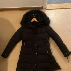 Svart lång dunjacka med fuskpäls - Säljer min fina Hollister jacka i storlek 34 (XS). Väldigt varm snygg modell - perfekt för vintern. Köpte för 5000kr säljer för 2500kr