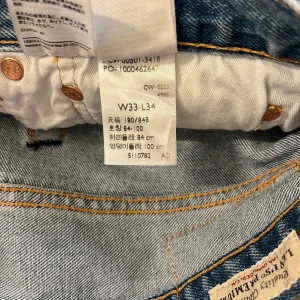 Levi's 501 ljusblå jeans W33 L34 - Klassiska ljusblå Levi's 501 jeans med raka ben och normal passform. Jeansen har fem fickor, knappgylf och den ikoniska läderpatchen bak i midjan. Tillverkade i slitstarkt bomullsjeansmaterial, perfekt för en avslappnad stil.