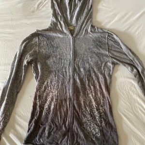 Grå hoodie med mönster från Oneworld - Grå hoodie från Oneworld med dragkedja och huva. Tröjan har blommigt mönster i vitt och grått framtill och på ärmarna. Strl M, fraktar gärna tillsammans med andra varor.