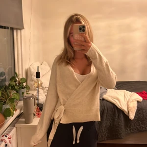 Beige omlottkofta från Esmara - Mysig beige omlottkofta från Esmara med knytband i sidan och v-ringad hals. Koftan är stickad och har långa ärmar, perfekt för lager-på-lager under kyliga dagar. Enkel och stilren design som passar till det mesta. Helt oanvänd!