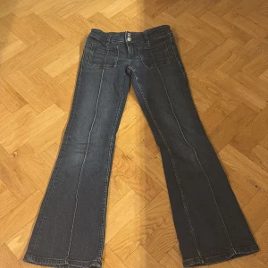 Blå bootcut jeans från Gina Tricot - Snygga blå bootcut jeans från Gina Tricot med markerade sömmar framtill och stora fyrkantiga fickor. Jeansen har dubbla knappar i midjan och klassisk femficksdesign. Perfekt för dig som gillar en retroinspirerad look med lite utsvängda ben.