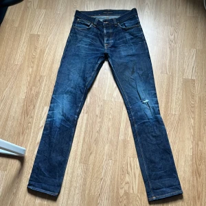 Nudie jeans grim Tim  - Jag säljer ett par sparsamt använda nudie jeans i modellen Grim Tim! Jeansen har fått en snygg wash och har även några schyssta slitningar som är en del av modellen. Den enda defekten är en liten svart färgfläck som knappt märks av vid användning. Storlek 32/34 sitter mer som 31/34.