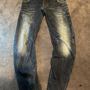 G-Star RAW blå jeans med detaljer - Snygga blå jeans från G-Star RAW med slitna detaljer och markerade sömmar. Jeansen har klassisk femficksdesign, kontrastsömmar och coola faded effekter framtill och baktill. Märkespatch bak i midjan och logga på fickan. Perfekta för en streetinspirerad look.