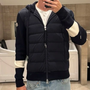Moncler mörkblå cardigan  - Snygg mörkblå jacka från Moncler med quiltad dunfront och stickade ärmar samt huva. Ärmarna har vita detaljer och dragkedja på sidan. Jackan har hel dragkedja framtill och en clean, sportig look som funkar till jeans och sneakers. Storlek L , kan gå ner i pris🤗
