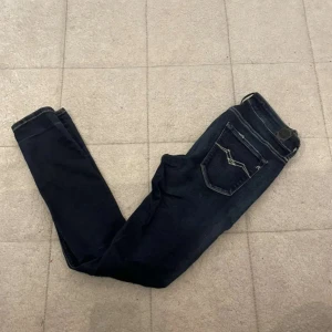 Mörkblå Replay jeans slim fit - Snygga mörkblå jeans från Replay med slim fit och klassiska fem fickor. Jeansen har diskreta slitningar och kontrastsömmar på bakfickorna. Perfekta för dig som gillar en stilren och modern look. W27 L30