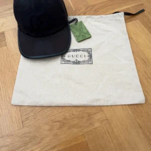Gucci keps - Snygg svart keps från Gucci med diskret GG-monogram över hela kepsen. Kepsen har böjd skärm, justerbar rem bak och är tillverkad i bomullsmix. Perfekt accessoar för en trendig och exklusiv look.